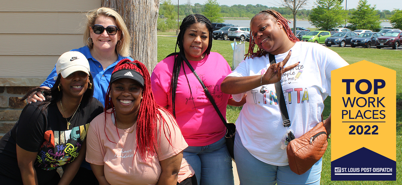 A group of four African American women and one white woman dressed casually and posing at an outdoor event